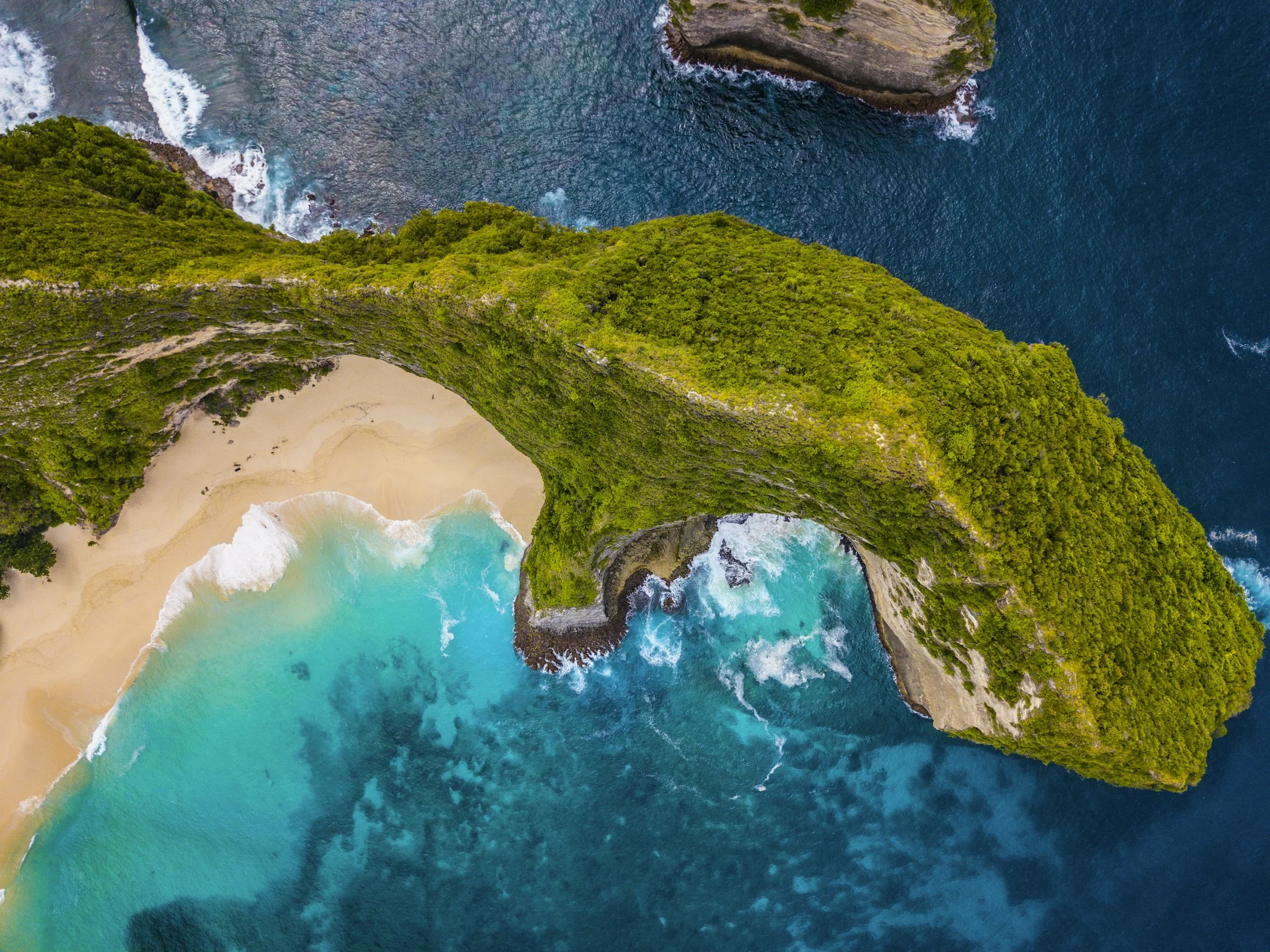 Aerial view of a green coastal cliff, sandy beach and turquoise water in Bali